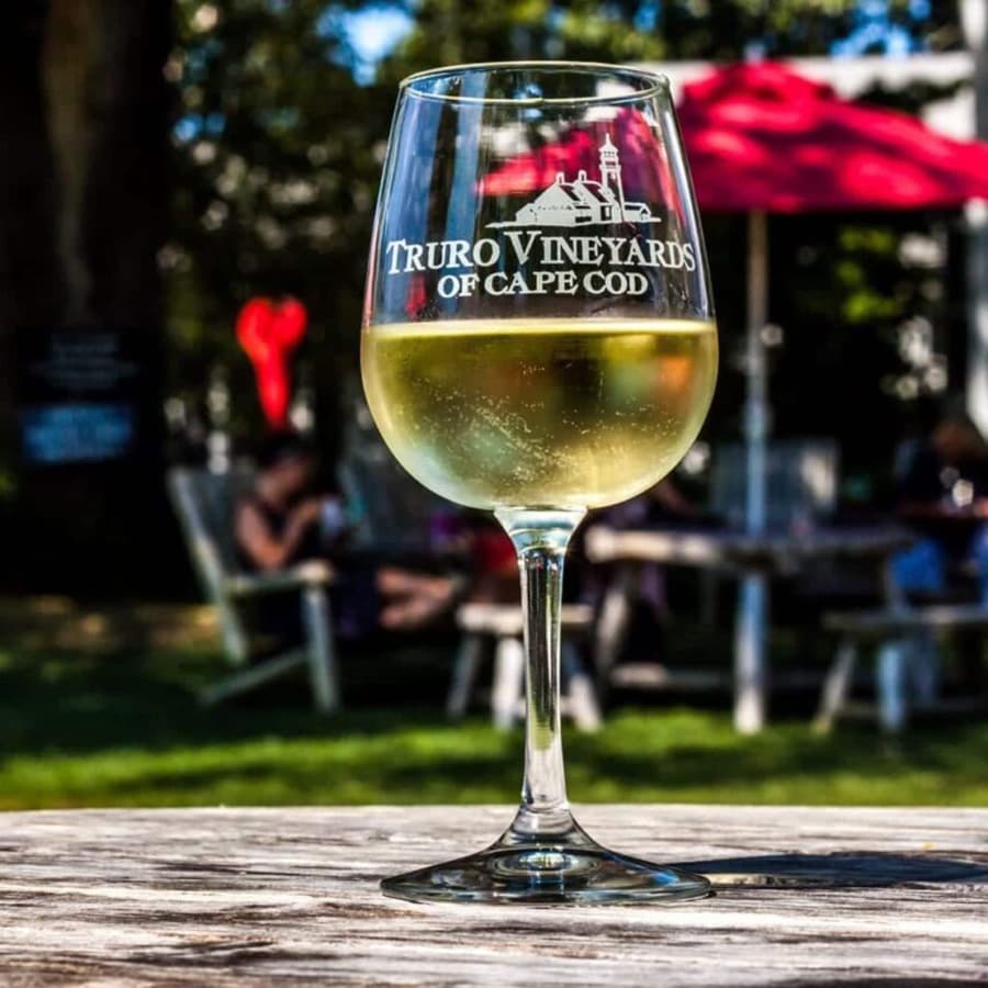 A glass of white wine from Truro Vineyards of Cape Cod sits on a wooden table in a garden setting.