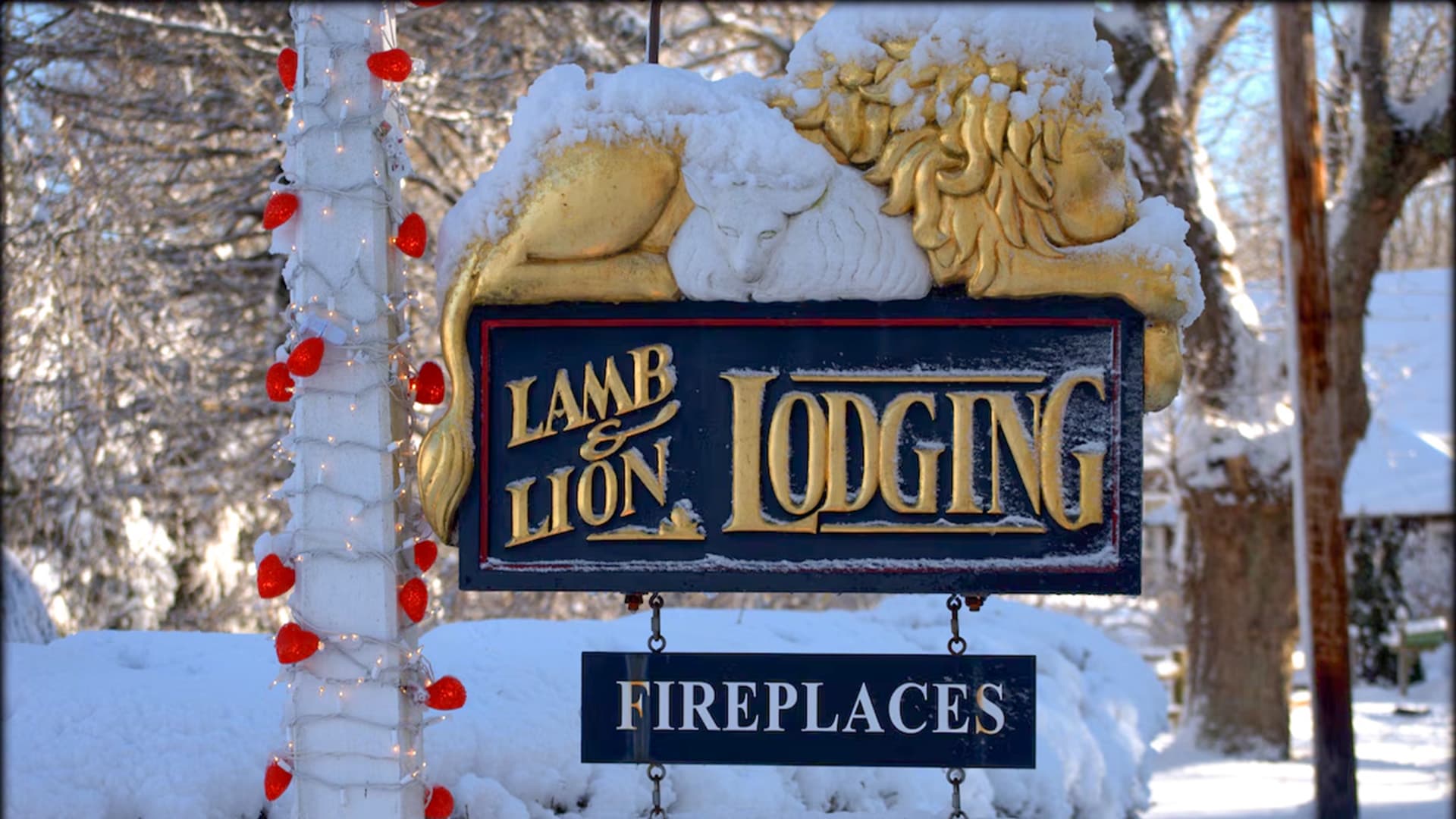 A snow-covered sign for "Lamb & Lion Lodging" with decorative lights and the word "Fireplaces."