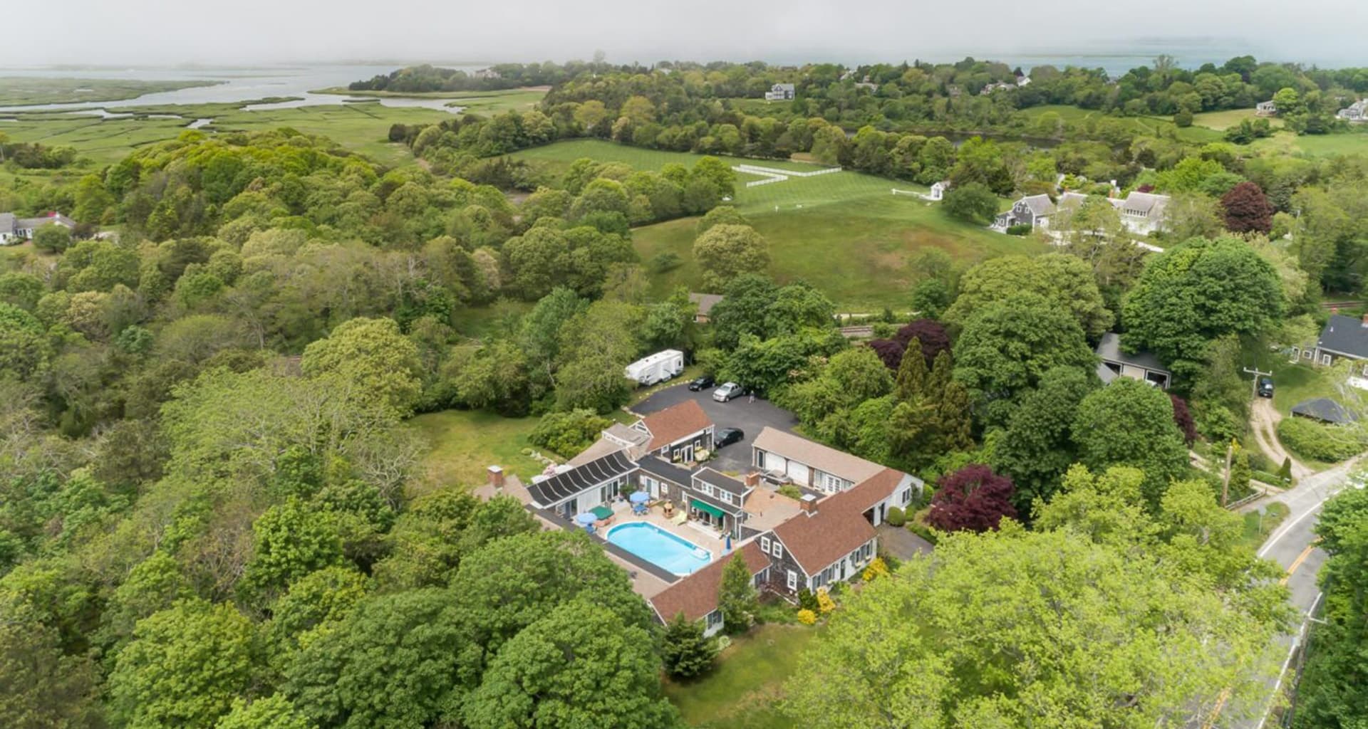 Aerial view of a residential property with a pool surrounded by lush greenery and fields.