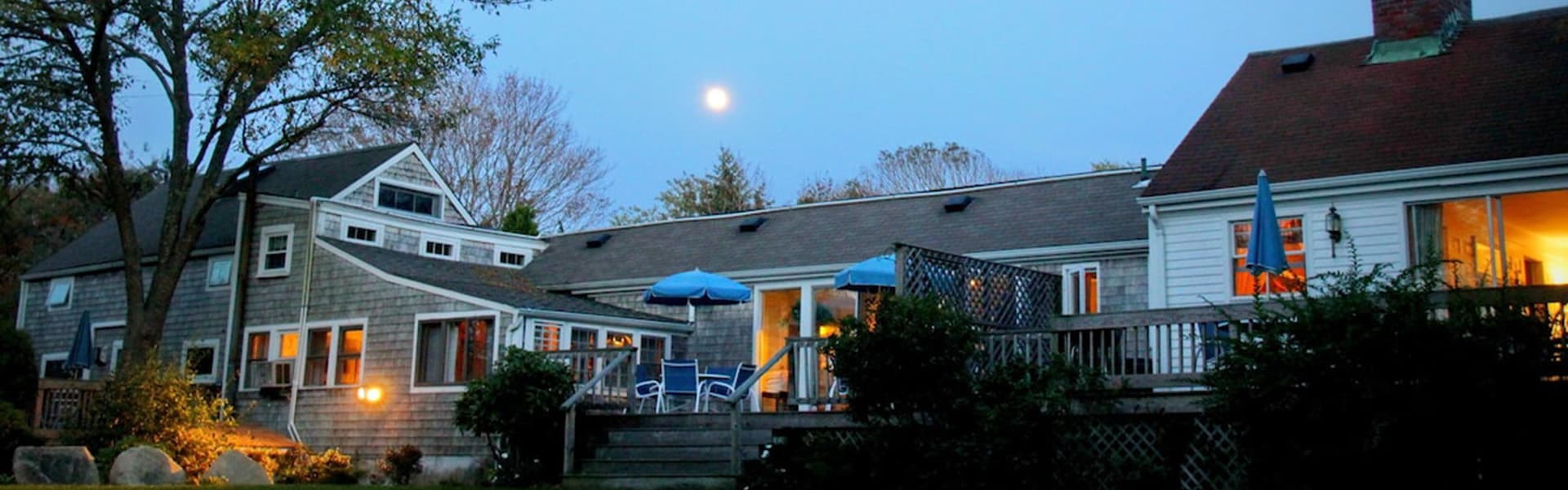 A cozy, illuminated house exterior with a full moon in the evening sky.