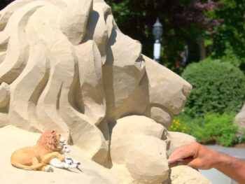 Sand sculpture of lion and man's hand by lamb being sculptured